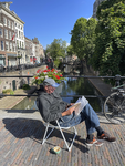 903604 Afbeelding van ontwerper en beeldend kunstenaar Kees Wennekendonk met een boek en een kopje koffie op een stoel ...